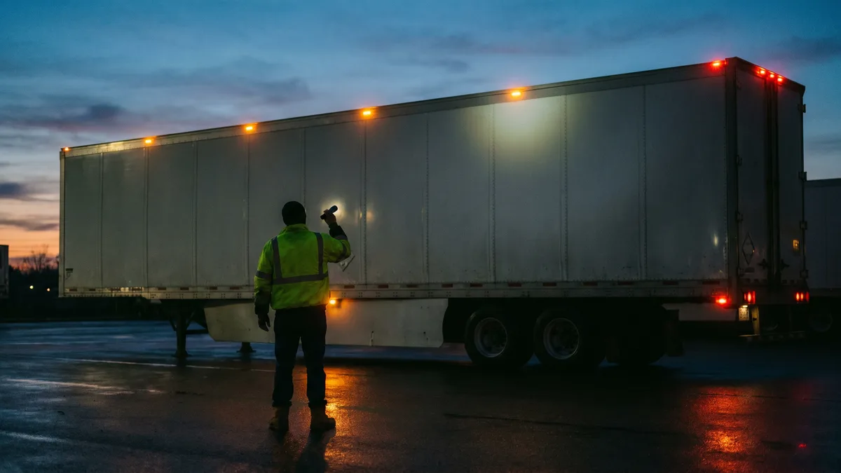 Driver doing a dusk walk-around with a flashlight checking trailer clearance and marker lights, a small habit that prevents one of the top reasons trucks fail safety inspection in Ontario